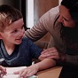 Young boy sitting at a table writing with smiling mom looking over his shoulder