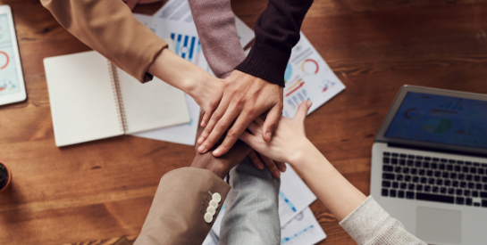 Multiple hands stacking together over a desk in a team huddle