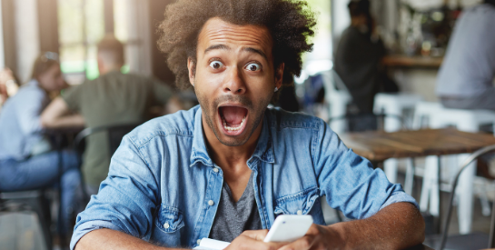 Black man with an excited face holding his cell phone in a coffee shop