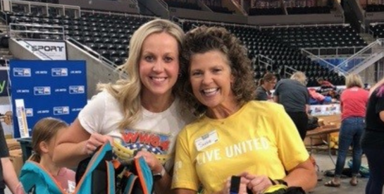 Two smiling women volunteers holding backpacks at the school supply drive