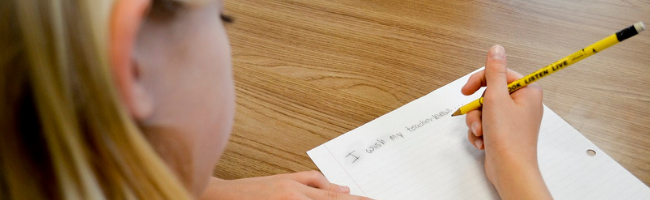 young girl student sitting at her desk with a pencil in her hand writing on a piece of paper