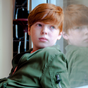 Serious looking red haired young boy looking out a window in school_Isaac