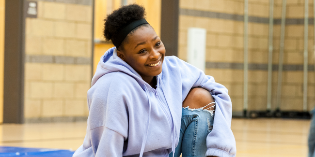 Smiling teen wearing a purple sweatshirt sitting on school gymnasium floor, Kylie