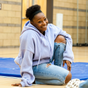 Smiling teen wearing a purple sweatshirt sitting on school gymnasium floor, Kylie